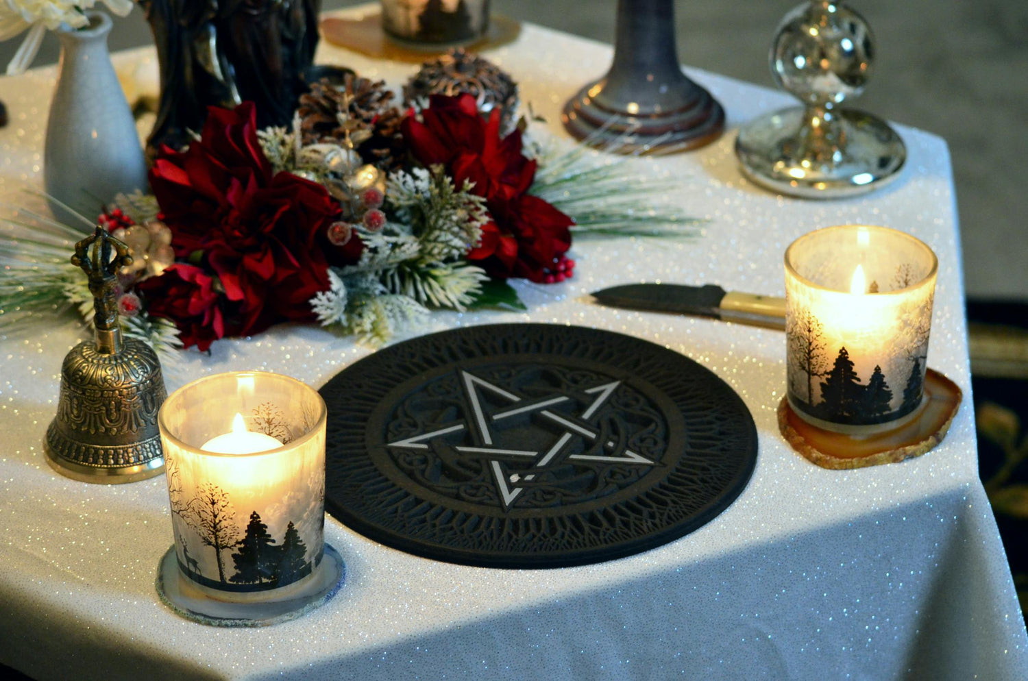 Photo of someone's altar including a pentacle slipmat, two candles, a bell, an athame, and red and silver faux flowers