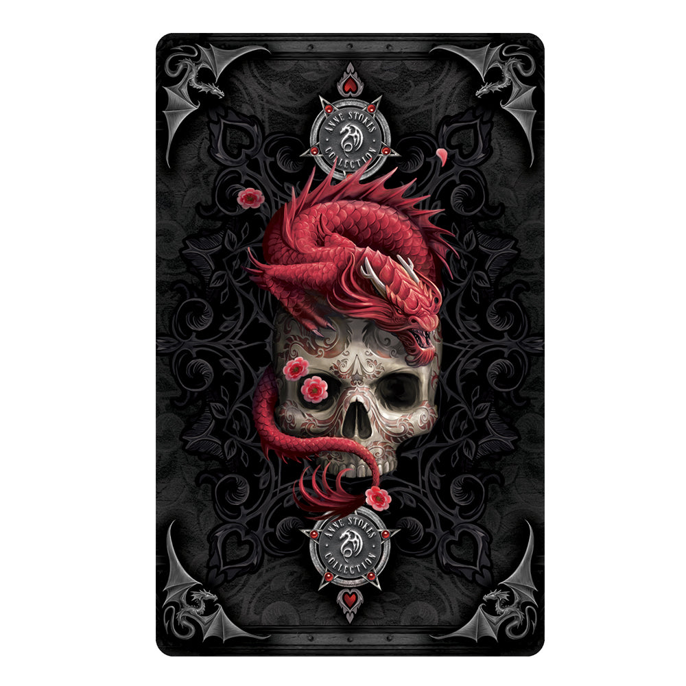 Back of card detail for Anne Stokes Gothic Oracle Deck cards. A gothic black background featuring hearts within clubs with four silver dragons adorning the card edges. The center is filled with a tattooed skull, its right eye covered with a red flower and atop the skull is a red dragon. Emblems top and bottom are the Anne Stokes Collection.